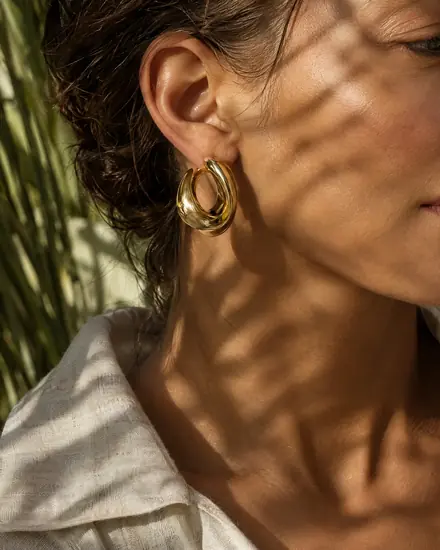 Gold hoop earring in warm sun and palm shadows